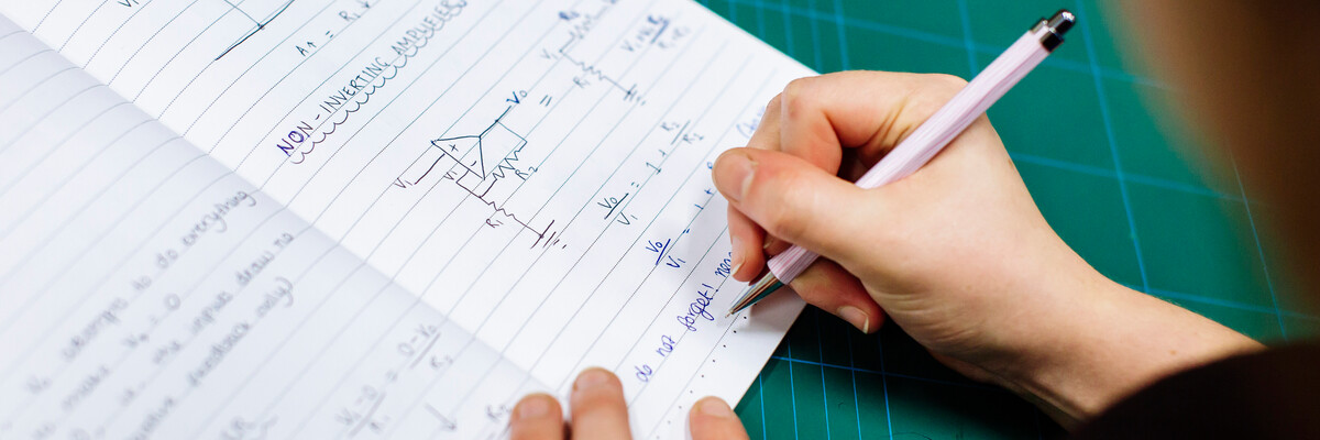 A person writes mathematical equations and electrical forumlae on a notebook.